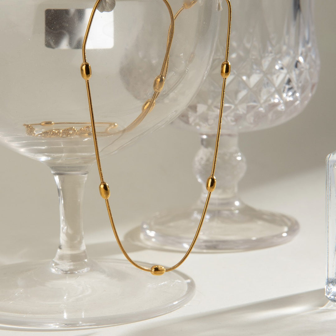 Gold Dainty Bead Necklace draped over a glass, showing the oval beads