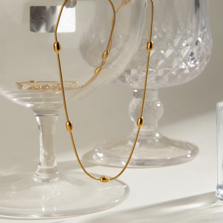 Gold Dainty Bead Necklace draped over a glass, showing the oval beads