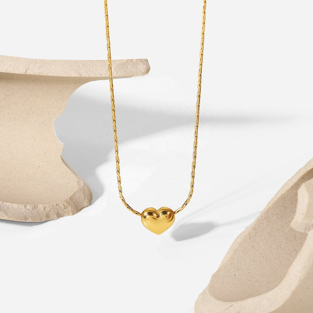 Gold Mini Heart Necklace hanging between two stone props