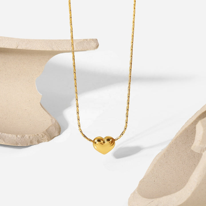 Gold Mini Heart Necklace hanging between two stone props