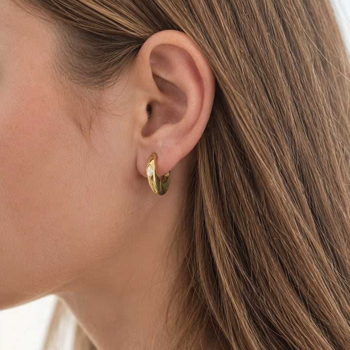 Gold Mini Solitaire Huggie worn on the earlobe, showing true size